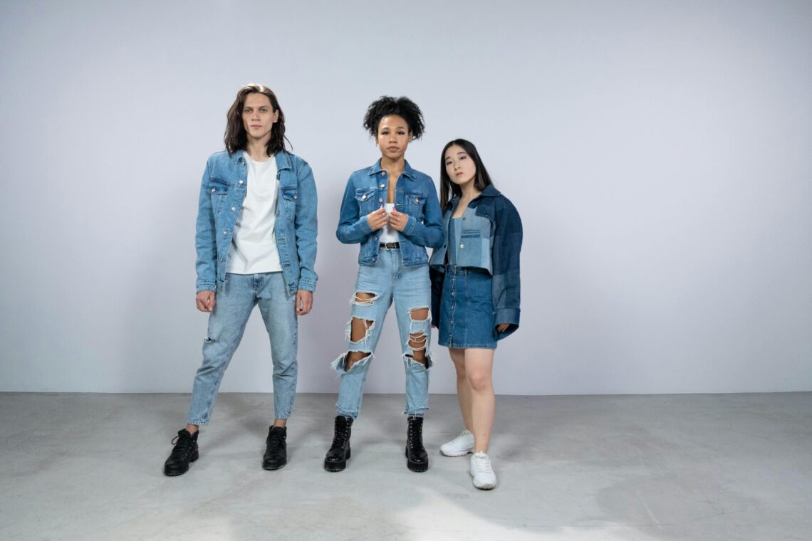 Young woman modeling a trendy denim mini skirt paired with a cropped patchwork denim jacket and white sneakers, standing alongside two others in full denim outfits. Perfect inspiration for casual mini skirt fashion
