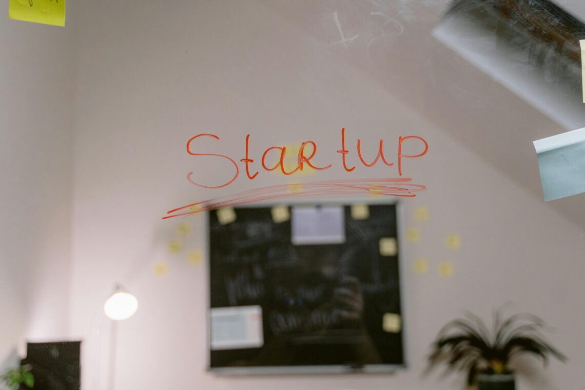 The word ‘Startup’ written in red on a glass board in a modern office setting, surrounded by sticky notes and planning tools—representing the brainstorming and innovation process of a startup business environment.