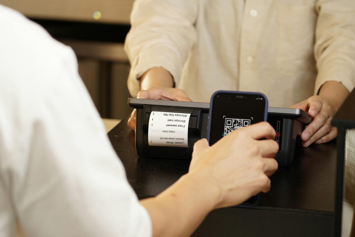 Customer scanning QR code with smartphone for e-wallet payment at checkout.