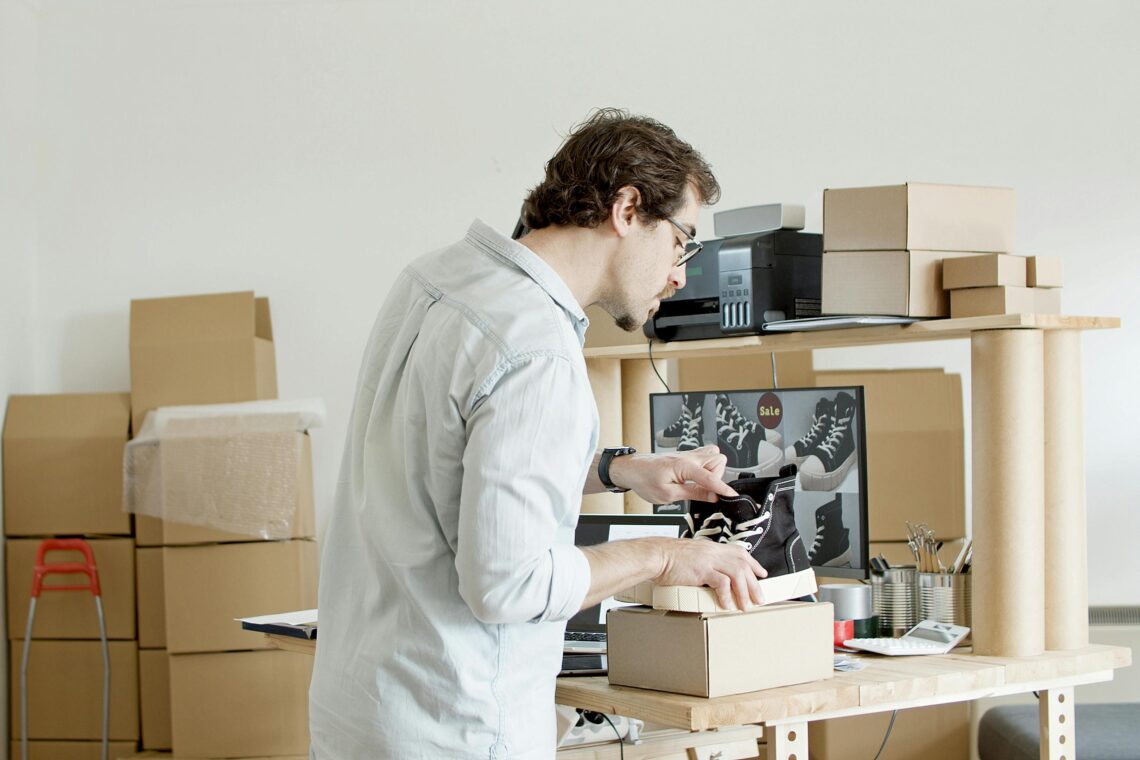 Entrepreneur packaging shoes for online orders in a small workspace with boxes and shipping supplies, representing the early stages of starting an online business.